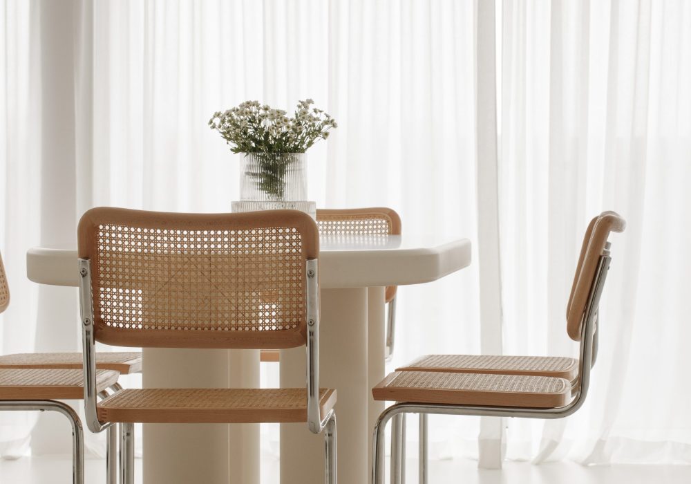 Interior of light dining room with white table, rattan chairs. Japandi interior concept